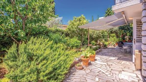 En uteplats med stenbeläggning och utemöbler, omgiven av frodig grönska och en pergola som ger skugga.