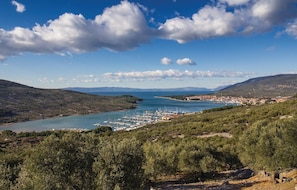 A coastal town with a marina, surrounded by hills and olive groves.