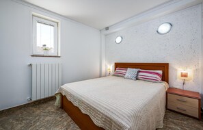 A bedroom with a bed, bedside table, wall-mounted light, radiator, and a window with a view. - Awesome Home in Baderna With Wifi and 2 Bedrooms (Porec)