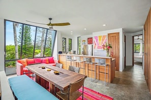 A modern kitchen with a bar area, large windows, and a dining space with a wooden table and chairs.