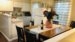 A compact kitchen with white cabinets, a refrigerator, a microwave, and a dining area with a wooden table and chairs.