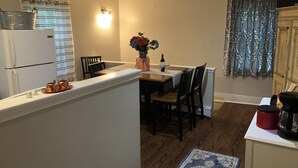 A kitchen with a dining area, wooden flooring, a refrigerator, a coffee maker, and a vase with flowers.