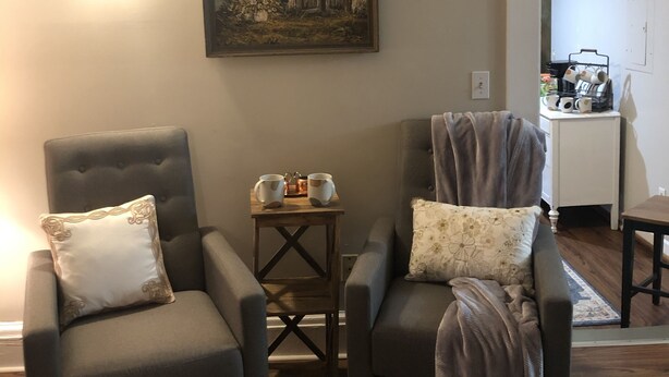 A living room with two grey armchairs, a small wooden side table, and a painting on the wall.