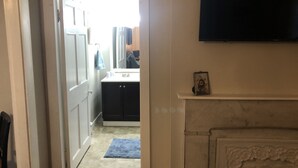 A hallway leading to a bathroom with a sink, a blue rug, and a framed picture on the wall.