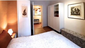 A hotel room with a bed, a nightstand, a chair, a wardrobe, a mirror, and a door leading to a bathroom. - Right in the middle and yet quiet (München)