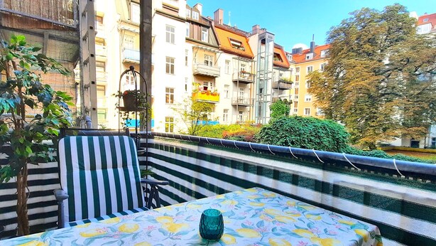 A balcony with a striped chair and a table with a floral tablecloth. - Right in the middle and yet quiet (München)