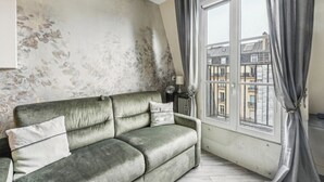 A living room with a grey sofa, a window with curtains, a lamp, and a wall with a floral pattern. - Studio Mac Mahon - Champs Elysees by B'Your Home (Paris)