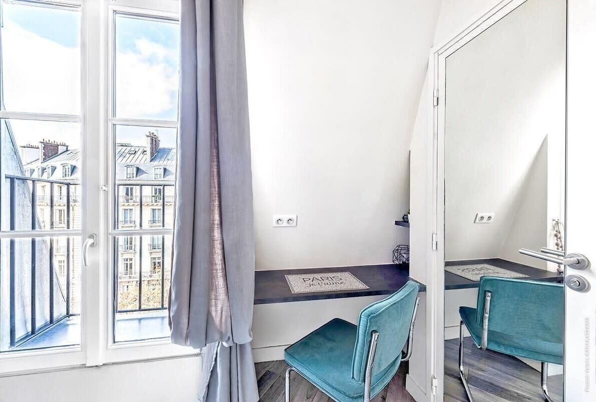 A compact room with a large window, a small table, two chairs, and a mirror.