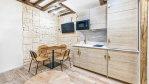 Eine kleine Küche mit Steinwand, Holzschränken, einer Mikrowelle und einer Essecke mit rundem Tisch und Stühlen.