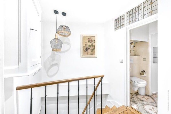 A staircase with a wooden handrail and metal balusters, leading to a bathroom with a toilet and a sink. - Grands Boulevards - Vivienne 1bdr (Paris)
