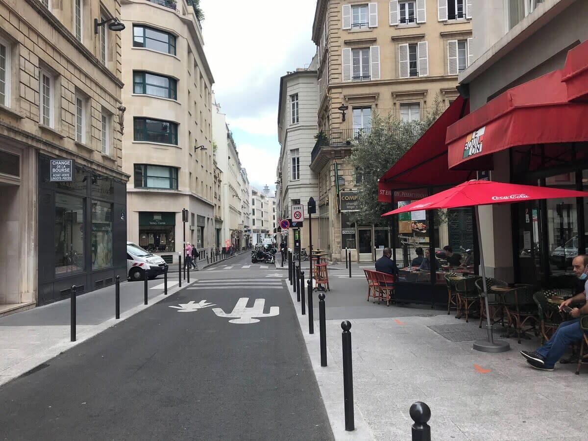 Une rue avec une piste cyclable, des immeubles et des espaces aménagés pour s’asseoir à l’extérieur.