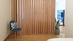 A room with a wooden slat partition, a blue chair with a patterned cushion, a white bed, and a potted plant. - Oceanus Executive Apartamento (Ponta Delgada)