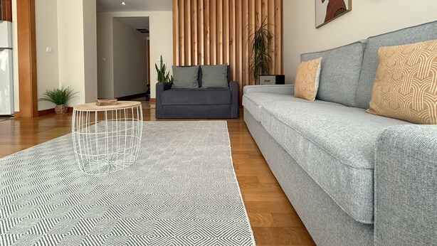 A modern living room with a grey sofa, patterned rug, and wooden panel wall. - Oceanus Executive Apartamento (Ponta Delgada)