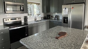Een moderne keuken met grijze kastjes, een roestvrijstalen koelkast, een magnetron en een granieten aanrecht.