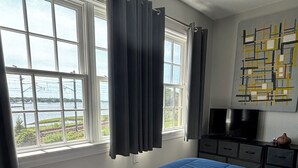Een slaapkamer met een groot bed, een televisie en uitzicht op een wateroppervlak door de ramen.