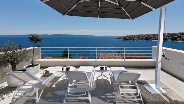 Eine Terrasse mit weißen Liegestühlen, einem Tisch mit Getränken und Blick auf das Meer.