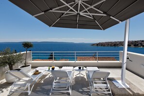 A terrace with white lounge chairs, a table with drinks, and a view of the sea. - Villa Anadea (Okrug)