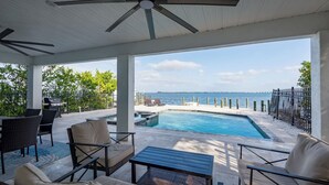 A covered outdoor area with a pool, seating, and a view of the sea. - Bay beauty with heated pool, spa, games, ping pong (Holmes Beach)