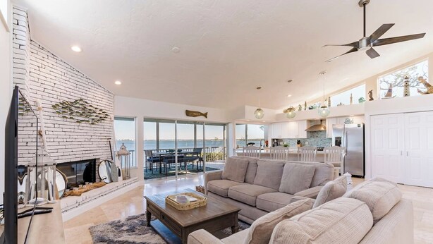 A spacious living area with a fireplace, a large sofa, and a dining area with a view of the sea. - Bay beauty with heated pool, spa, games, ping pong (Holmes Beach)