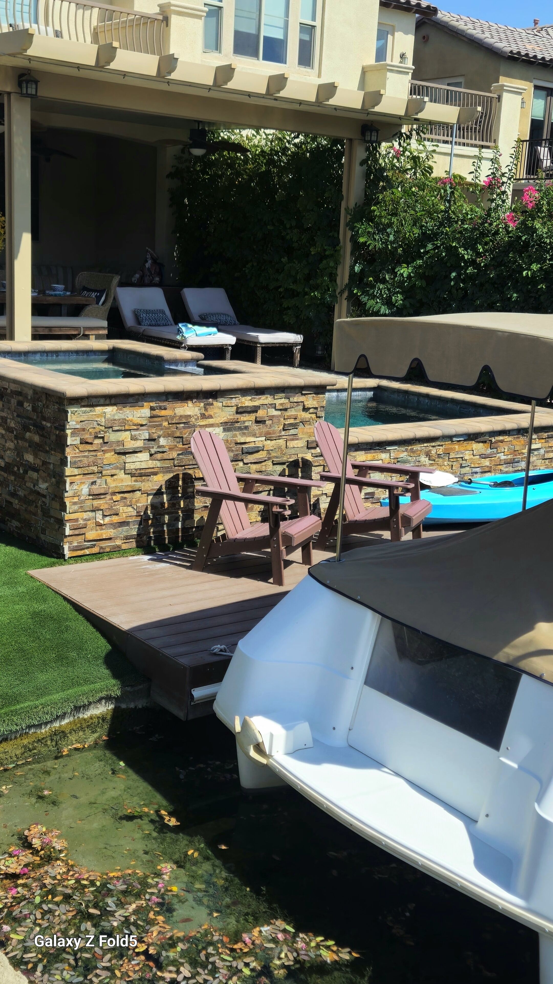 Ein Poolbereich mit Liegestühlen, einer Steinmauer und einer überdachten Sitzgelegenheit.