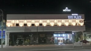 A hotel named 'VIVE PLACE' with a modern facade, illuminated windows, and a visible storefront below.