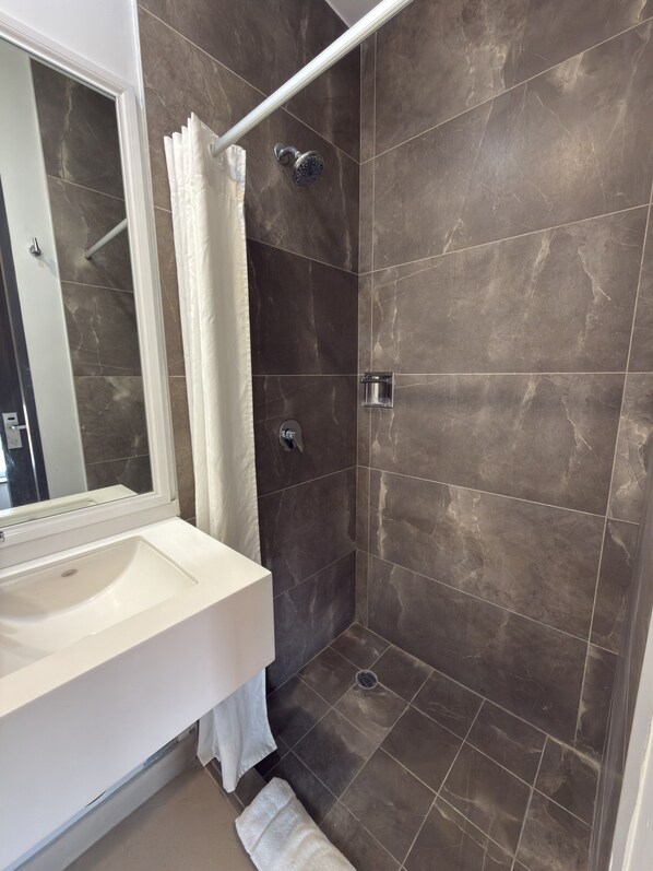 A bathroom with a white sink, a shower with a glass enclosure, and dark tiled walls.