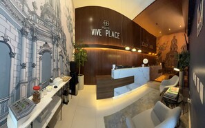 A hotel reception area with a modern design, including a reception desk, seating area, and a mural of architectural details.