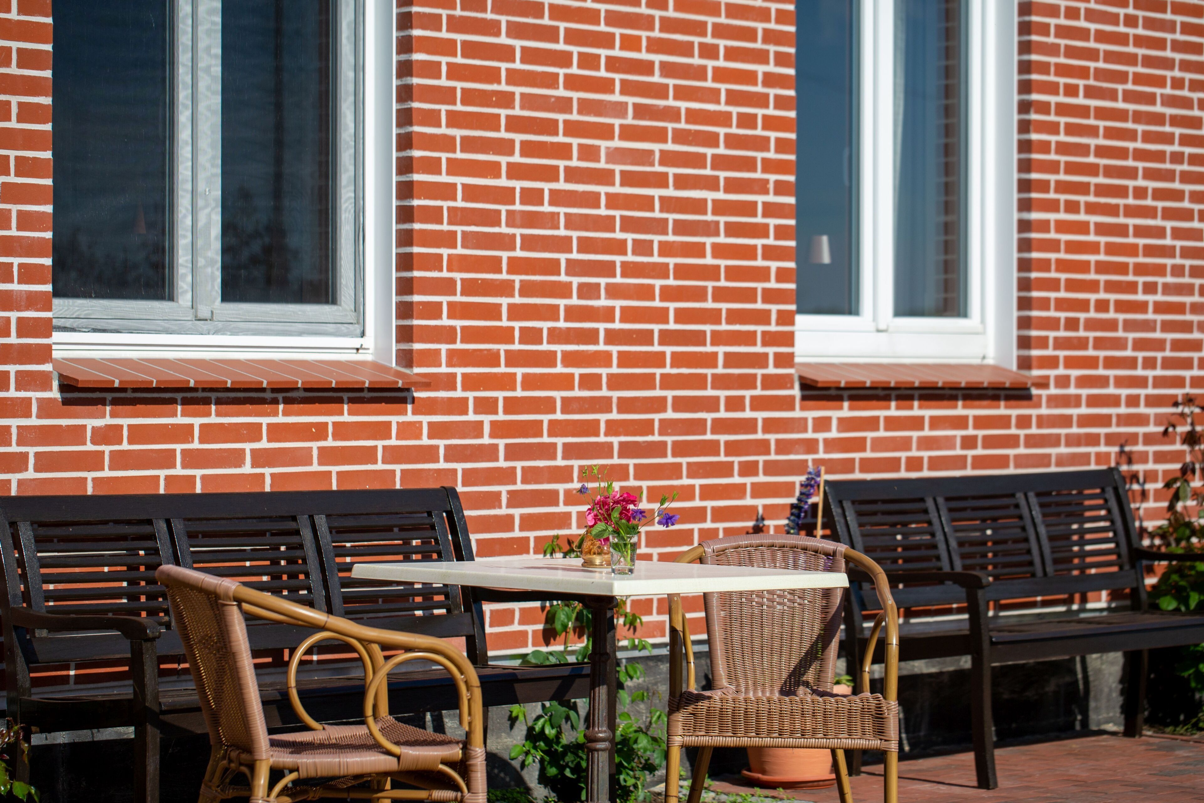 A patio with wicker furniture, a table with a vase of flowers, and a brick wall with windows.