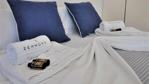 A neatly made bed with white linens and towels, two blue pillows, and two framed artworks on the wall. - Zennova 16 Naftilos Family Summer House (Kassandra)