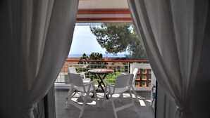 A balcony with two white chairs and a small table, overlooking a scenic view with a tiled roof and trees. - Zennova 16 Naftilos Family Summer House (Kassandra)