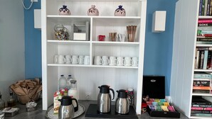 A kitchen with white cabinets, a coffee station, and a bookshelf with books and decorative items. - Studio (2 adults), Marias Place Oia (Thira - Santorini)