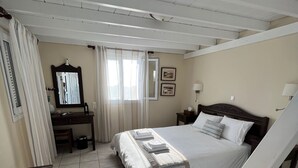 A bedroom with a bed, bedside tables, a desk, a chair, and a window with curtains. - Studio (2 adults), Marias Place Oia (Thira - Santorini)