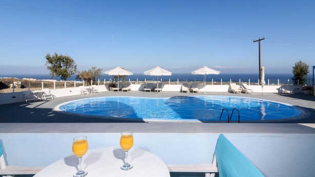 A poolside area with lounge chairs and umbrellas, a pool, and a view of the sea. - Studio (2 adults), Marias Place Oia (Thira - Santorini)