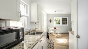 A kitchen with a granite countertop, stainless steel sink, and a microwave. There is a dining area with a white table and chairs. - Charming, Central Jamestown Cottage, walk to town/beach! (Jamestown)