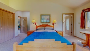 A bedroom with a wooden bed, two bedside tables, a nightstand, a window with a curtain, and a door leading to another room.