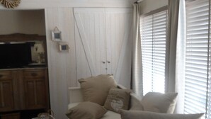 A bedroom with a bed, pillows, a radiator, a window with blinds, a television, and a wooden cabinet.