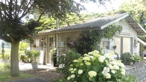 A stone building with a tiled roof, a garden with hydrangeas, and a sign reading "PASSE & PARTOUTAGE".