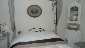 A bedroom with a four-poster bed, a bedside table with a lamp, a clock, and a window with curtains.
