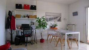 Een moderne kantoorruimte met een bureau, computer en bureaustoel. Een boekenplank met ordners en een potplant.