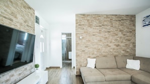 A modern living room with a flat-screen TV, a beige sofa, and a stone wall. - Modern House W.large Garden & Children Playground (Split)