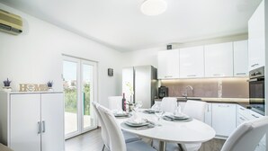 A modern kitchen with white cabinets, a dining table set for four, and a view of the outdoors. - Modern House W.large Garden & Children Playground (Split)