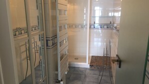 Een badkamer met een douchecabine van glas, betegelde wanden en een betegelde vloer.