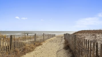 A sandy beach path with wooden fences on both sides leading to the ocean.