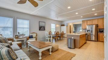 A spacious living area with a dining set, kitchen, and a ceiling fan.