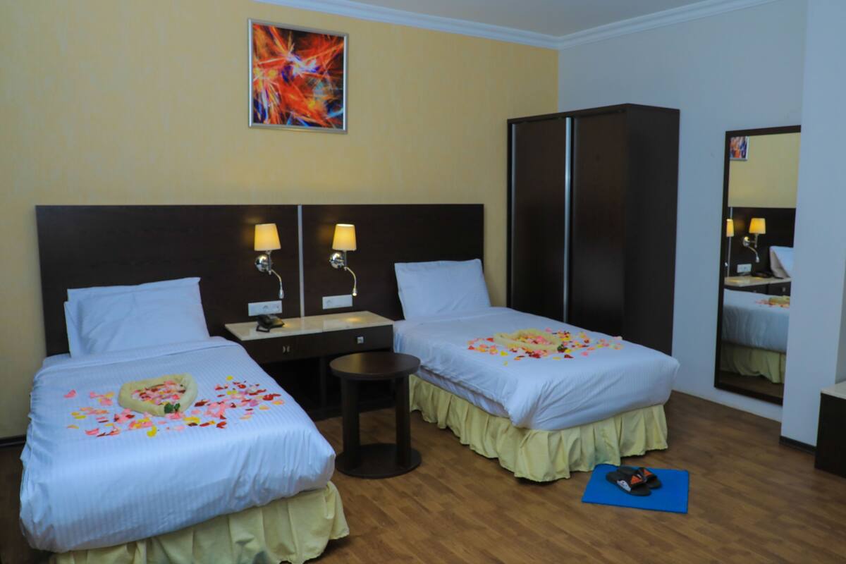 A hotel room with two beds, a desk, a mirror, and a wardrobe.
