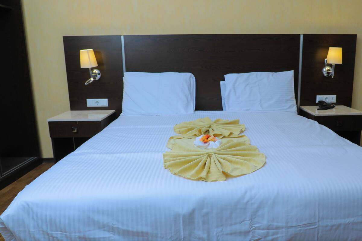 A hotel room with a large bed, two bedside tables, and two wall-mounted lamps.