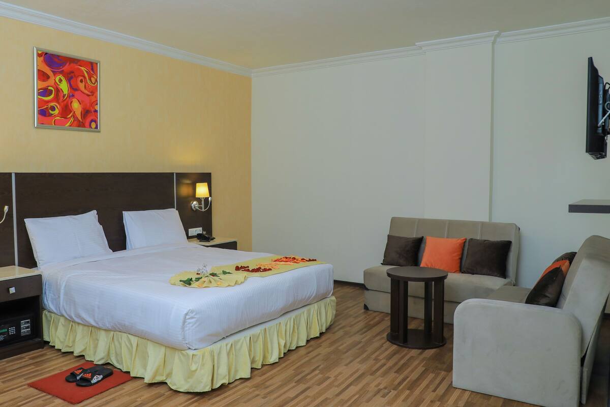 A hotel room with a large bed, bedside tables, a sofa, a small table, and a TV.