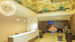 A modern reception area with a reception desk, a decorative light fixture, a digital screen, and a flower arrangement.