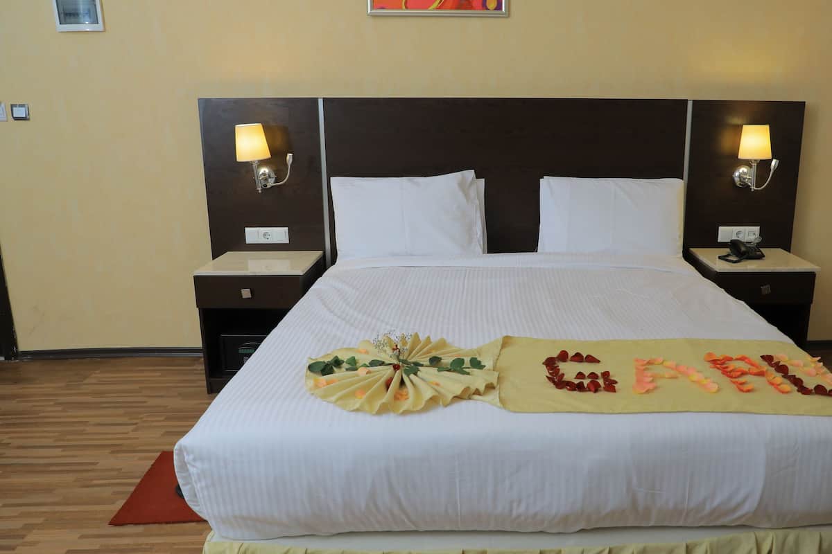 A neatly made bed with white linens, two bedside lamps, and a decorative pillow with a floral arrangement.