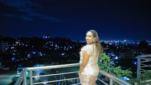 A person standing on a balcony overlooking a cityscape at night.